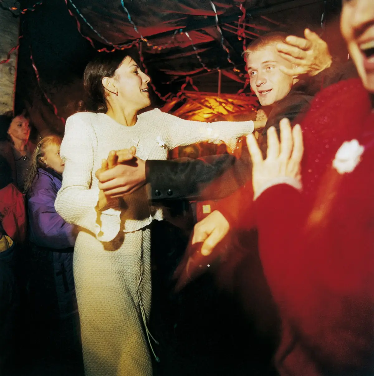Woman in white dress dancing with a man at a crowded indoor party with streamers.