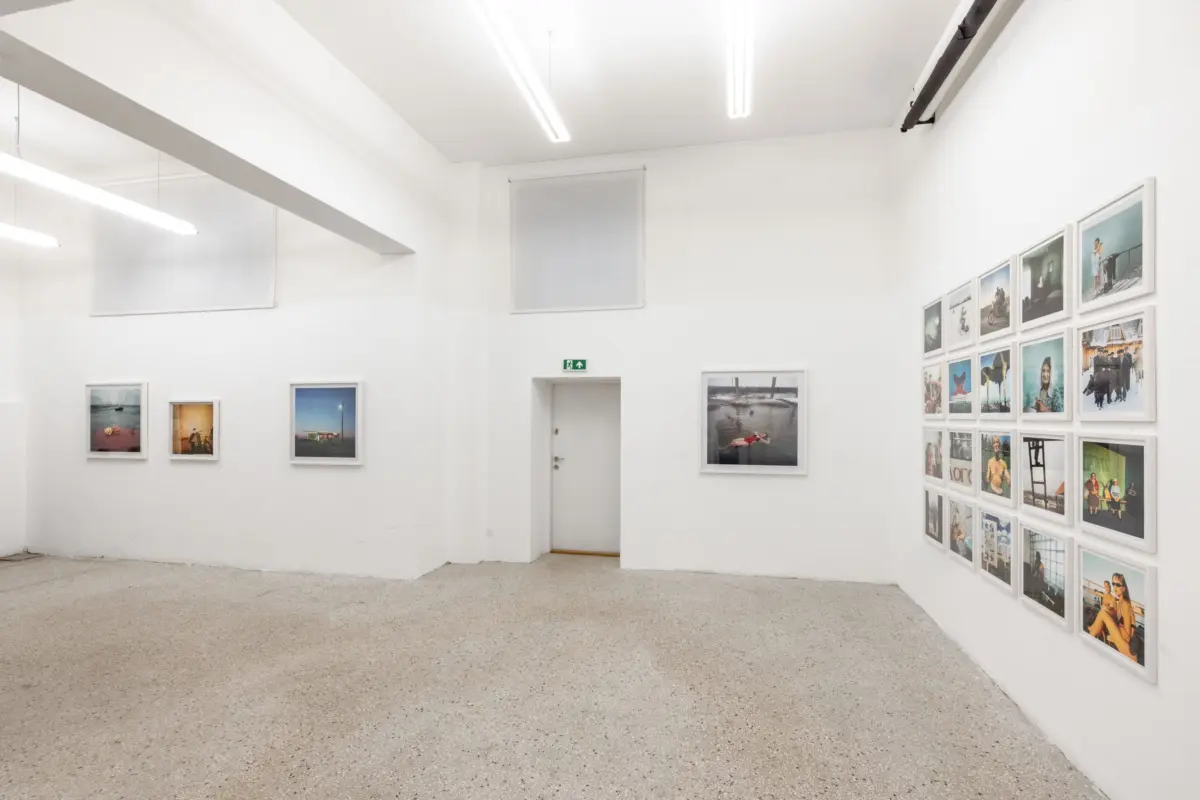 White-walled gallery interior with a grid of framed photographs on the right wall and several framed prints on the left.