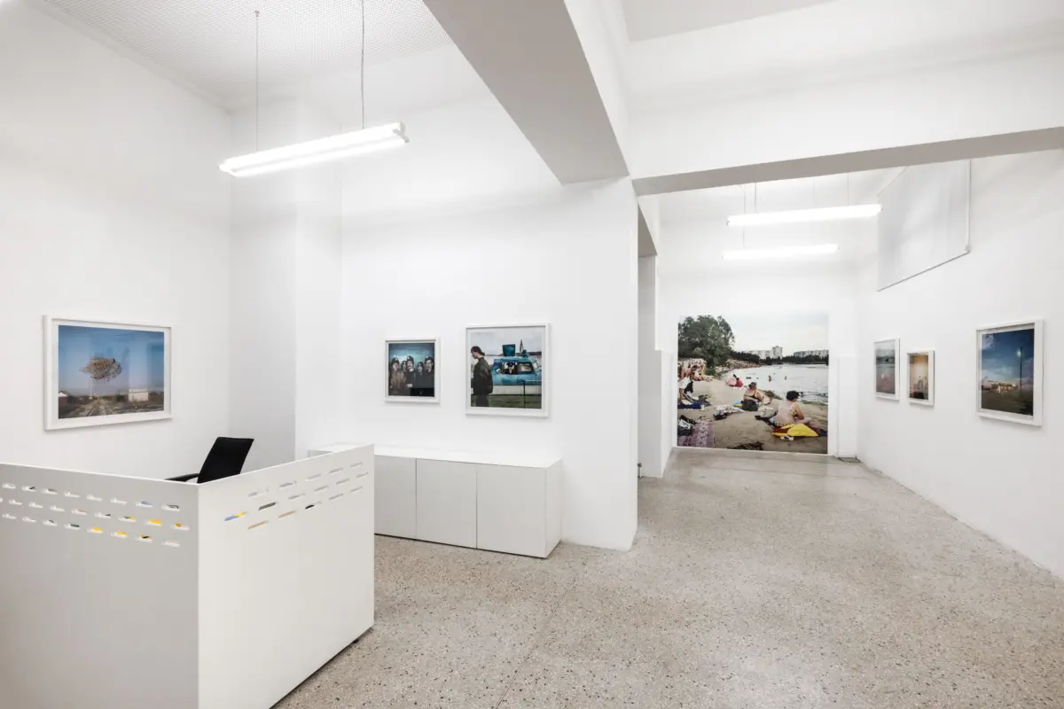 Bright white art gallery with framed travel photographs on the walls; white reception desk in the foreground.