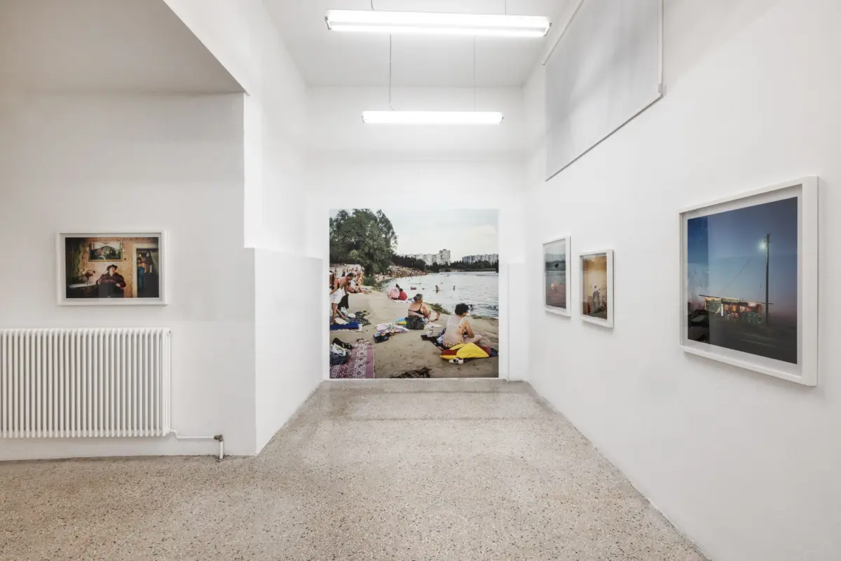 White-walled gallery hallway with framed landscape photographs; large beach scene at the far end.